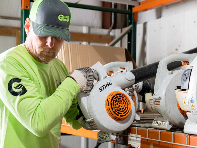 Green group employee picking up a leaf blower
