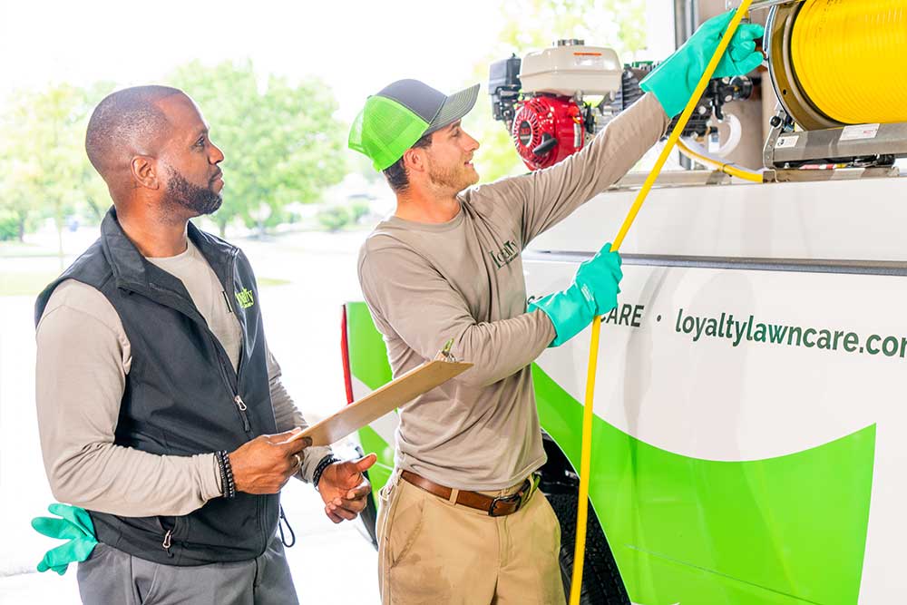 Two green group employees using equipment in the back of a truck